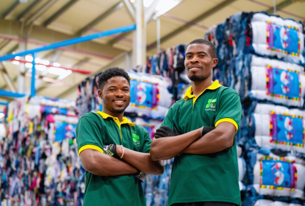 MS Group staff smiling in front of packed racks of used clothes bales