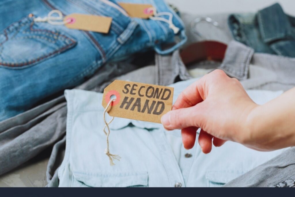 Hand inspecting label on second-hand jeans with visible "second hand" tag